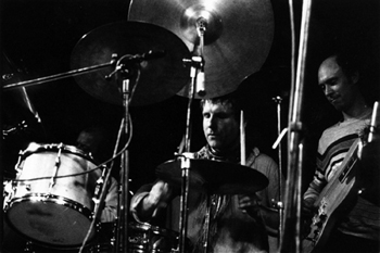 black and white photo of Pip Pyle playing drums and Richard Sinclair standing behind playing bass guitar