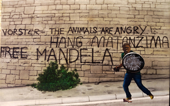 partheid era young man with stone to throw and bin lid sheild in front opff wall showing free mandela