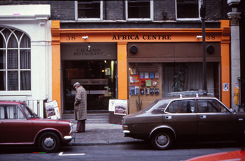 Colour photo taken in 1980 showing the outside of the Africa Centre and a man looking at a poster advertising the art attacks apartheid exhibition