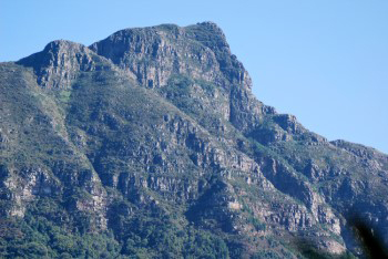 Devil's Peak under cool blue grey light showing green clad sandstone rocky outcrop layers.