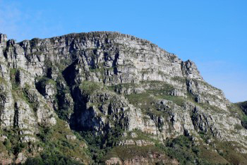 Harsh rugged craggy buttress outcrops showing pale grey sandstone layers and green patches of vegetation on the slopes.
