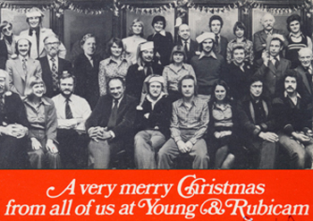 Black and white staff photograph featuring the words, A very merry Christmas from all of us at Young & Rubicam,showing a young Martin Lovis among a group of colleagues some wearing Santa hats.. 