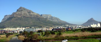 Panoramic view of the Table Mountain range under a clear pale blue sky with Cape Town city suburbs below and above the Black River.