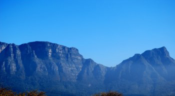 Panoramic distant view of Table Mountain east side Devil's Peak under blue green haze on a clear sunny day with clear blue sky overhead.