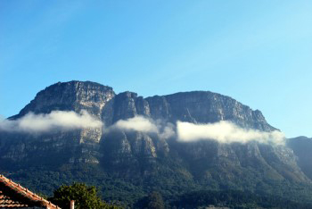 The mountain buttresses in the distance with a long narrow strip of white clouds about half way up the mountainside on bright sunny day.