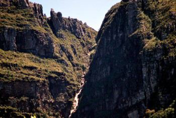 Close up view under morning light that has a red orange colouration with green vegetation covering most of the rocky outcrops of the buttress.