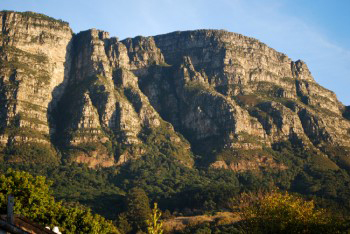 Warm sunlit bathed view over Newlands forest of four protruding buttresses and the shadow face has nose eys and forehead but lips not fully formed.
