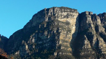 Fernwood and Protea buttresses swathed in warm sunlight under azure blue sky and shadow face almost fully formed to look more recognizeable as a face profile.
