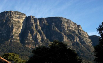 Craggy buttresses sit up proud in early morning sun showing deep shadows and the face changing shape again under a cool blue sky with high wispy white cirrus clouds.